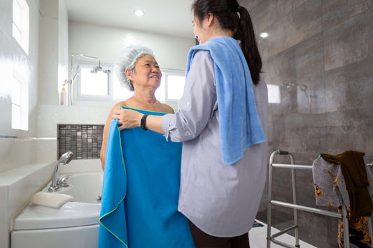 A woman in the bathroom helping a woman with her towel in a compassionate manner.